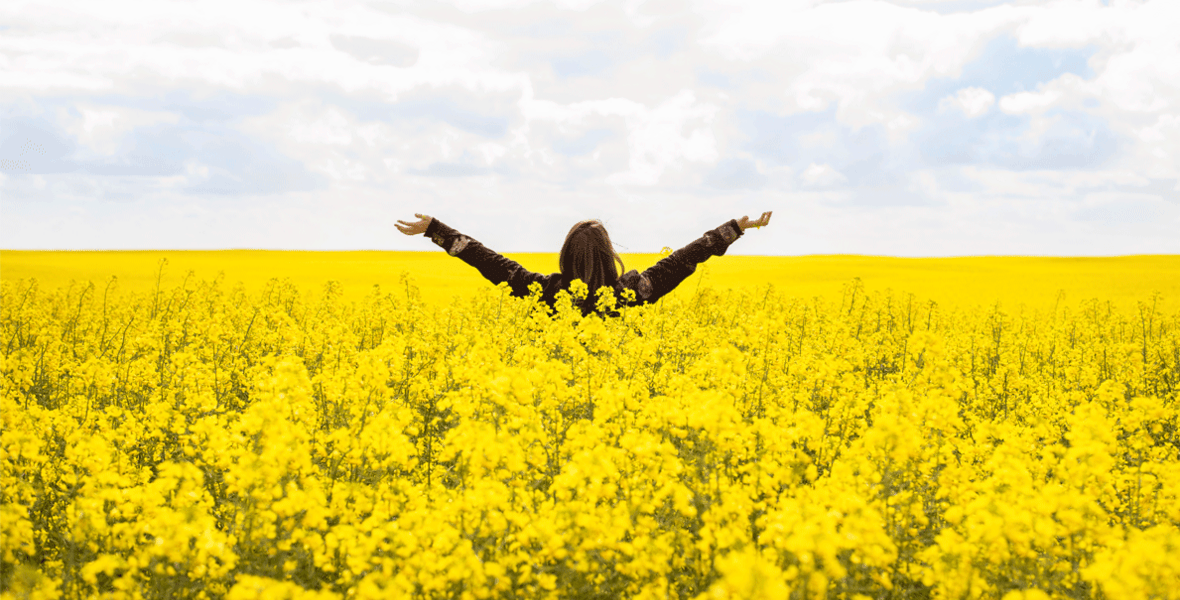 Rear view of a young woman with her arms raised skyward while standing in a field of canola in the springtime