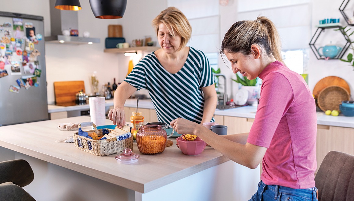 A young woman with hearing aids talking to her mother in the kitchen. They have a breakfast and enjoying the time they spending together.
