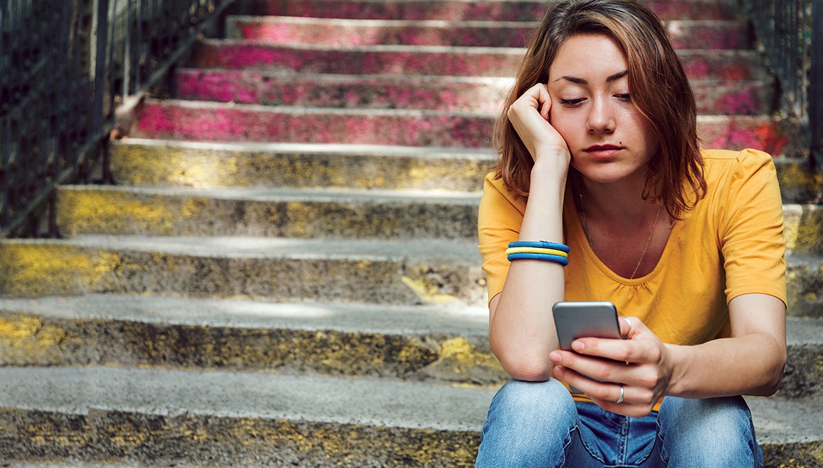 Teen girl dressed in yellow t-shirt sitting on stairs and is breaking up with her boyfriend through text messages.