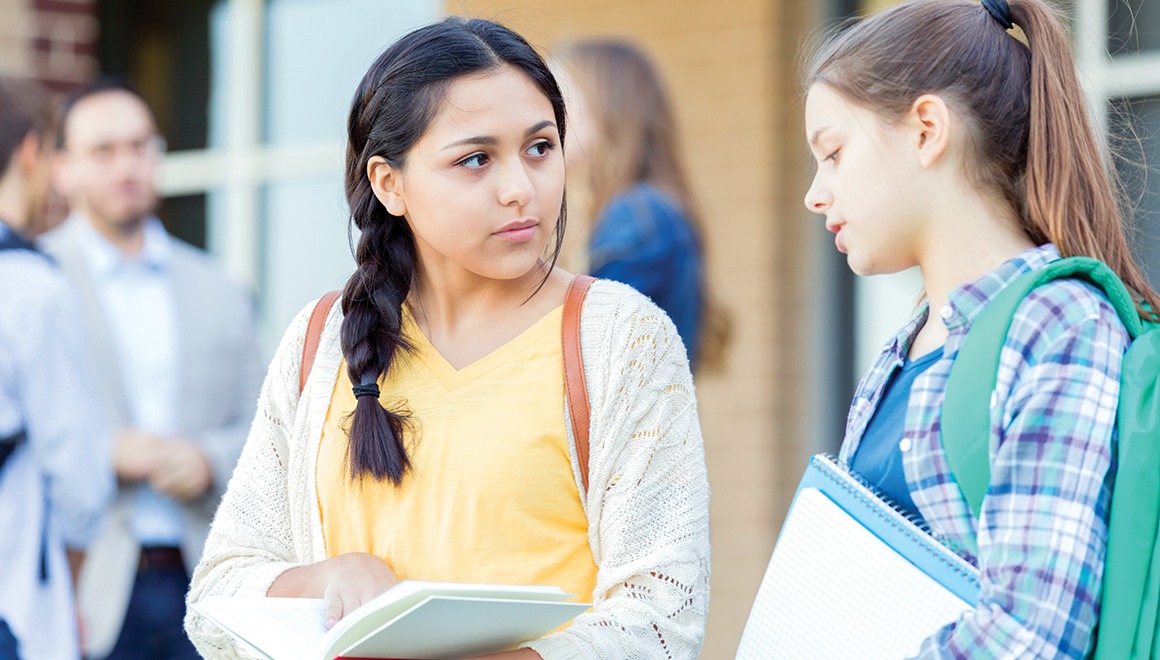 Serious teenage girls discuss an upcoming exam as they wait for school to start